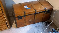 View of wooden chest with metal bands, lock plate, and handles. Shows scratches and wear on lid and sides.