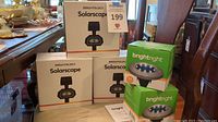 Five boxes of solar garden lights: two green Brightright boxes and three white/orange Brightology Solarscape boxes