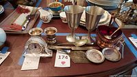 Full view of lot showing silver plated chalices, red glass serving bowl with ladle, crystal clock, silver cups, silver sugar bowl with spoon, serving pieces and coasters.