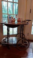 View of tea cart from side showing drop leaf top with attached items and wheels on sides