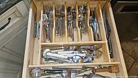 Wooden drawer organizer filled with multiple sets of Oneida flatware including forks, knives, spoons, and additional serving utensils.