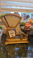 Vintage gold metal kitchen scale with semicircle dial, scratches and wear, with plastic fruit and vegetables on platform.