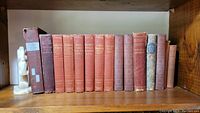 Full view of antique books on shelf, mostly with red/maroon covers, showing variety of titles.