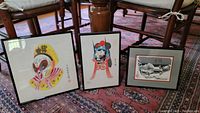 Three framed Asian art pieces resting on a carpeted floor, showing the different sizes and colorful theatrical prints alongside the black and white print.