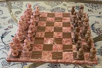 Top view of marble chessboard with complete set of pieces arranged at starting positions, showing the checkerboard pattern and polished natural stone pieces.