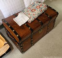 Wood steamer trunk style chest with several linens on top showing floral fabric and white embroidered linens.