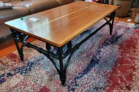 Front angle showing wooden top and black wrought iron base with decorative circular accents on the side
