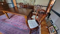 Six Nichols & Stone wooden dining chairs around a wooden table. Two captain's chairs with armrests and four straight chairs without. Cushions are light-colored and tufted.