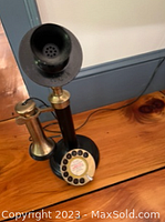 Early model candlestick telephone with black and brass finish, rotary dial with instructional label visible.