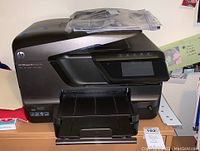 Front view of HP OfficeJet Pro 8600 Plus printer showing input and output trays, control panel and LCD screen. Printer is dark gray and black.
