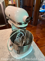 Front angle of white KitchenAid Heavy Duty stand mixer on marble counter with stainless steel bowl attached.