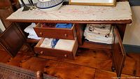 Wooden cabinet with drawers and doors open showing folded linens, tablecloths, towels in white and neutral colors with some embroidery visible.