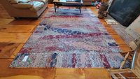 Full view of the multicolored area rug on rustic wooden floor, showing the pattern and size.