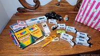 Photo displaying assortment of model cars, Crayola markers and crayons, Bicycle playing cards, scissors, and small craft items on a wooden surface.