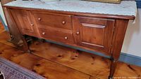 Front view of wooden sideboard showing drawers and cabinet doors with wooden knobs, placed on wooden floor with decorative cloth on top.