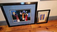 Photo showing both framed silk embroidery art pieces on a wooden surface against a neutral background.