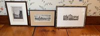 Three vintage framed engravings on a wooden surface, each depicting architectural cityscape scenes.