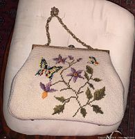 Front view of vintage embroidered handbag showing floral and butterfly needlework on cream fabric.