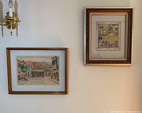 Photo showing both framed artworks hanging on a wall: the Zvi Ehrman watercolor on the left and the Judaica print on the right.
