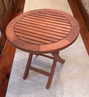 Front angled view of round wood slat side table with folding legs.