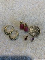 Photo showing all jewelry items including one pair of hoops, two small pink stone earrings, two small pendants with colored stones next to a quarter for size reference.