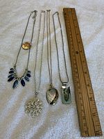 Four vintage pendants and chains laid flat next to a ruler for size reference.