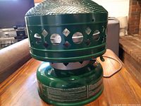 Green metal vintage Coleman heater shown on wooden table; decorative circular cutouts visible along firewall.