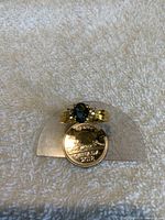 Front view of the gold tone ring with a dark blue stone, displayed with a coin for size reference.