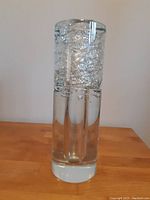 Full view of the clear crystal cylindrical vase with internal bubble texture on a wooden surface against a plain background.