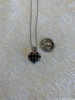 Pendant necklace shown beside quarter coin for size comparison, highlighting pendant cluster of garnet stones and silver setting.