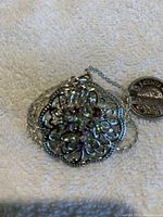 Front view of round silver flower pendant with colored stones on silver chain, displayed next to a quarter for size reference.