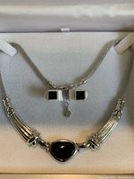 Pendant necklace and matching earrings arranged in a jewelry box, showing silver-tone metal and black stones.