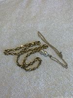 Photo of both the pearl necklace and the silver chain with double pearl pendant laid out on a textured light surface.