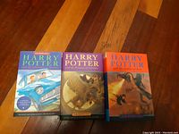 Three Harry Potter books with colorful illustrated covers shown together on a wooden floor.