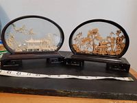 Full view of both oval cork dioramas on wooden surface with tape measure for scale, showing black lacquered stands and natural cork carving details through glass