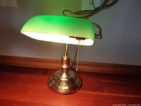 Vintage bankers lamp with green glass shade illuminated, showing full lamp and pull chain