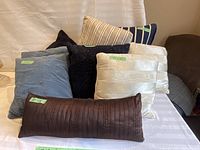 Front view of assorted throw cushions arranged showing various textures and colors including light blue, navy, cream, and brown.