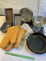 Overview of bakeware including loaf pans, springform pans, Bundt pan, oven mitts, tea towels, and jar