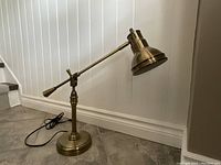 Full side view of brass desk lamp with adjustable arm and round weighted base, cord visible.