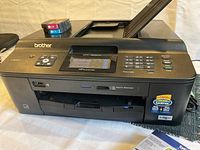 Photo of Brother printer with display screen, keypad, and paper trays visible