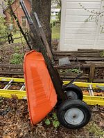 Side view showing orange steel tray, steel frame, dual pneumatic wheels, handles