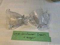 Photo of creamer and sugar bowl set placed on a white textured cloth with a green note 'Lot 2 - Cornflower Cream & Sugar'