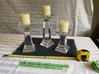 Three cut glass candle holders on table with ivory pillar candles. Tape measure and green tape label with measurements visible.