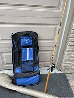 Fishing gear backpack standing upright in front of garage door next to fishing rod and cloth case on ground