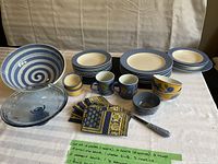 Photo of the blue and yellow patterned dishes, bowls, mugs, napkins, serving bowl, display dish and knife arranged on table.