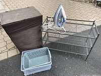 Overall photo showing laundry basket, metal shoe rack, bins, and iron on outdoor paving