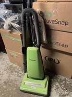 Front view of green Panasonic upright vacuum showing body and attached hose with handle.