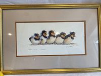 Framed print of five baby birds on a branch with open beaks, viewed at an angle, showing gold metal frame and cream matting.