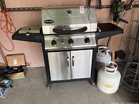 Full frontal view of Patio Chef gas barbecue with side shelves, control panel, and two propane tanks beside it on floor.