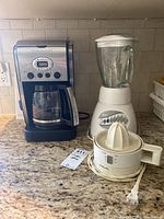 Three small kitchen appliances on countertop: Cuisinart coffee maker, Oster blender, Philips juicer